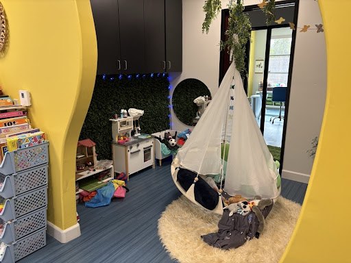 A hanging cocoon swing under fairy lights, next to a play kitchen and a living green wall